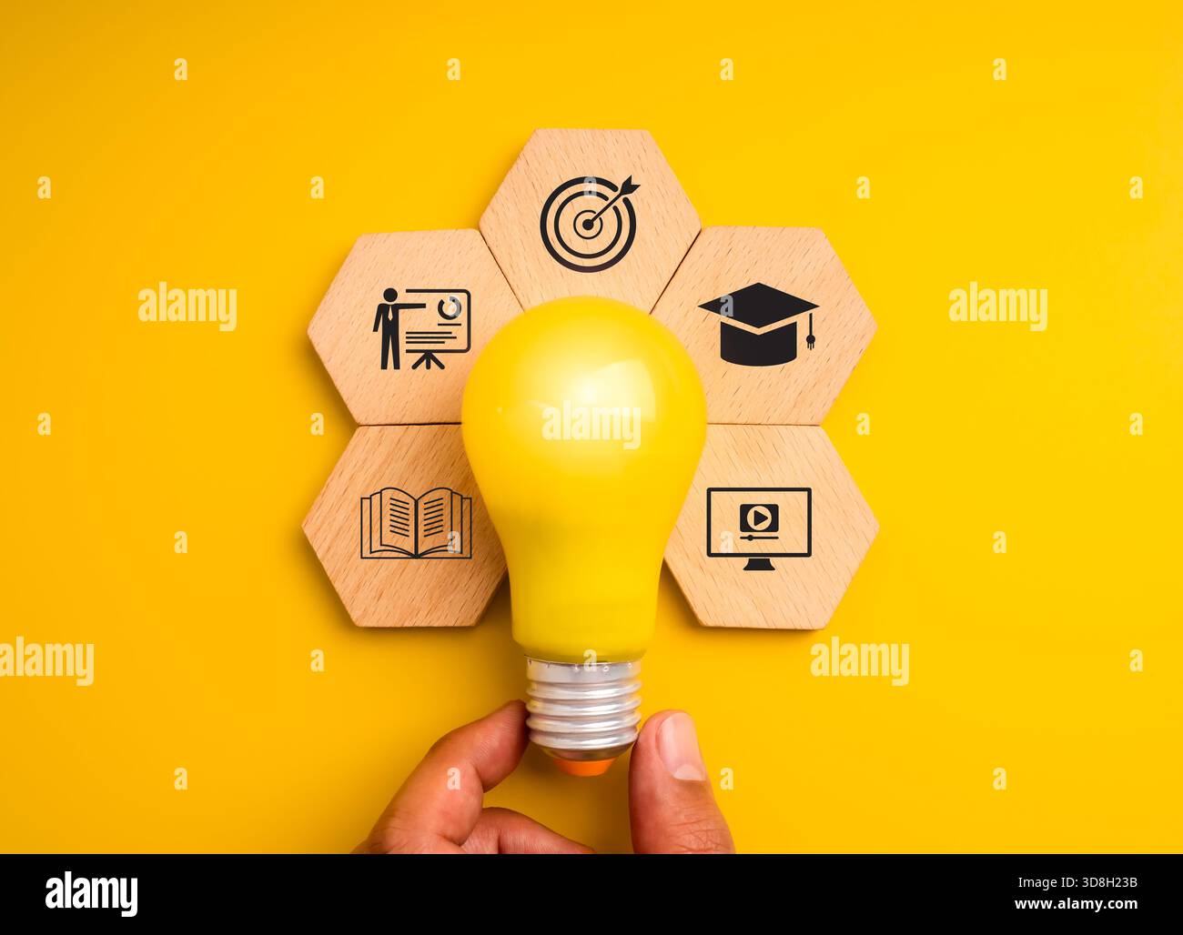 Gelbe Glühlampe mit Symbolen für Lernen, Training und Bildung auf sechseckigen Holzblöcken symbolisiert Wissen, Kreativität und E-Learning. Ideal für m Stockfoto