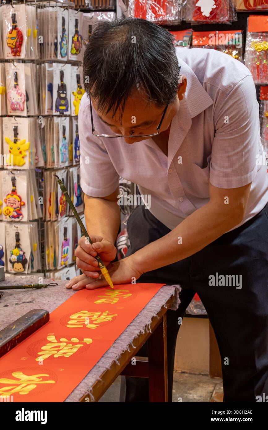 Er malt Goldkalligraphie chinesisches Schriftzeichen auf rotem Papier Stockfoto