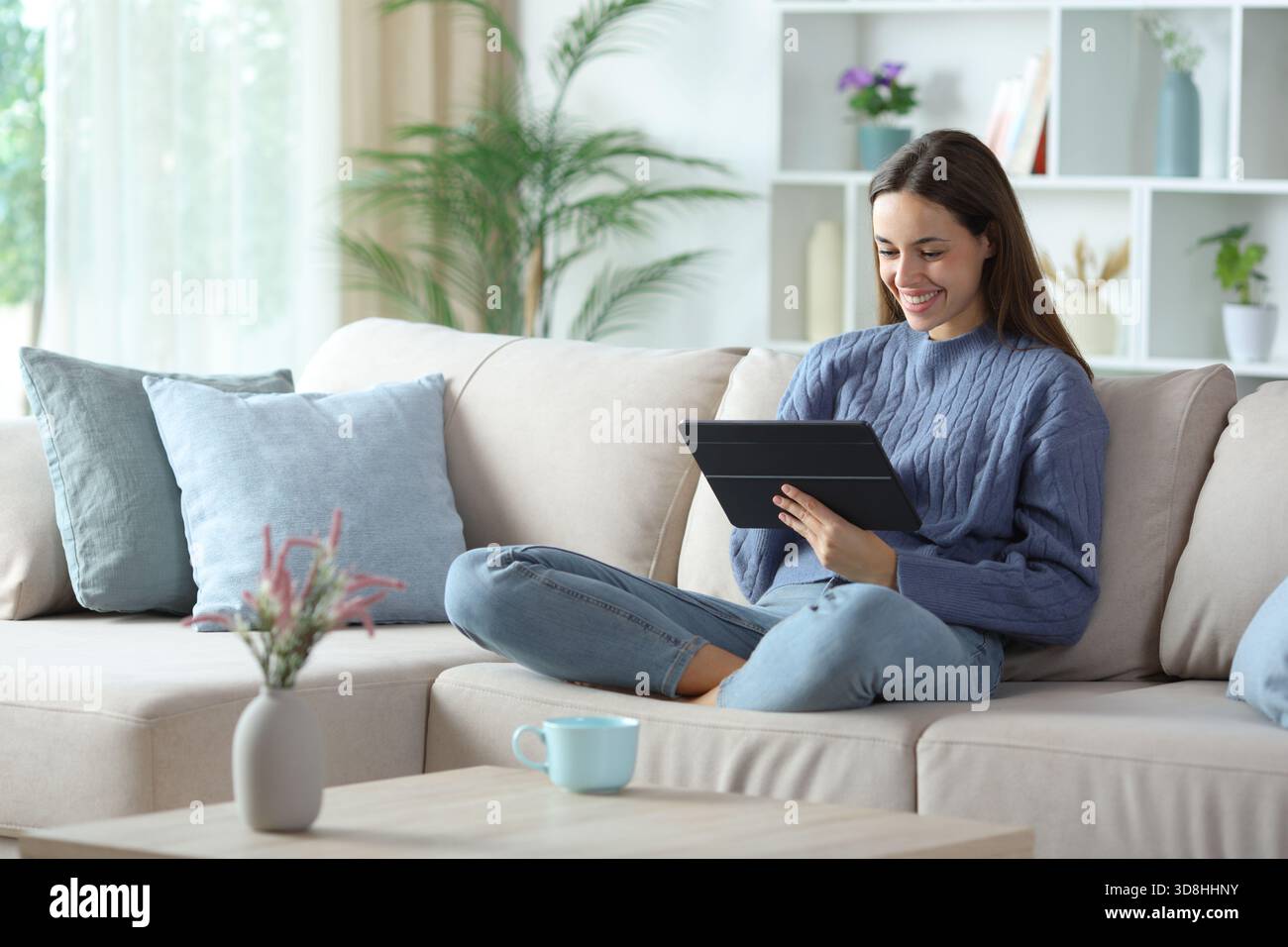 Glückliche Frau in Blau, die zu Hause auf einer Couch sitzt Stockfoto