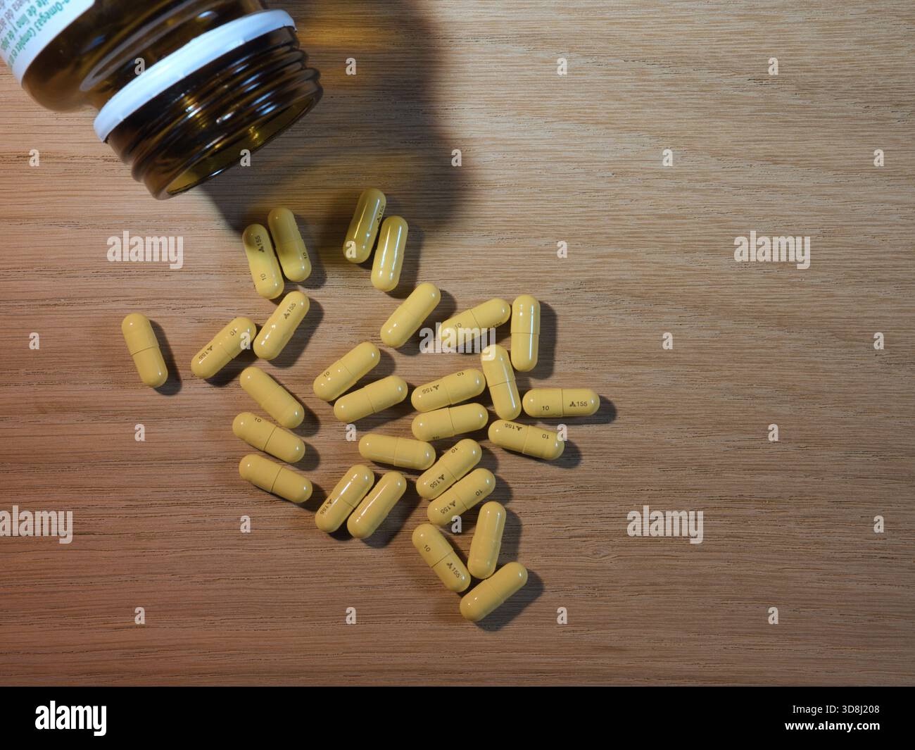Medikamentenkapseln und Flasche auf Holz - gelbe Kapseln verschüttet von einer braunen Arzneimittelflasche auf einem hellen Holztisch. Steht für Gesundheit, Medikamente, Stockfoto