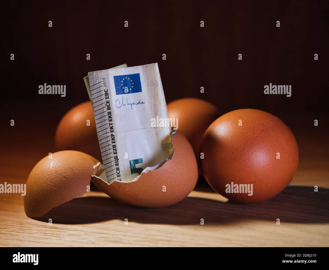 Fünf-Euro-Banknote in Broken Eggshell – Eine fünf-Euro-Banknote, die von einer gebrochenen Eierschale auf einem Holztisch auftaucht. Symbolisiert Einsparungen, Investitionen und neue f Stockfoto