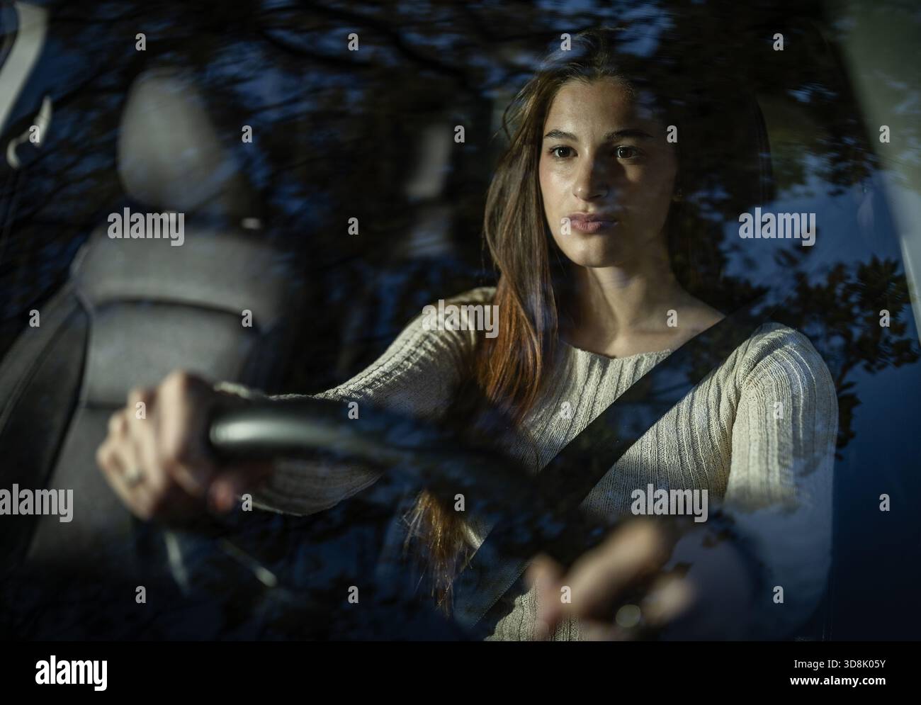 Die junge Frau fährt ihr Auto in der Dämmerung, konzentriert sich auf die Straße vor Ihnen. Das warme Licht verstärkt die ruhige Atmosphäre des Abends. Stockfoto