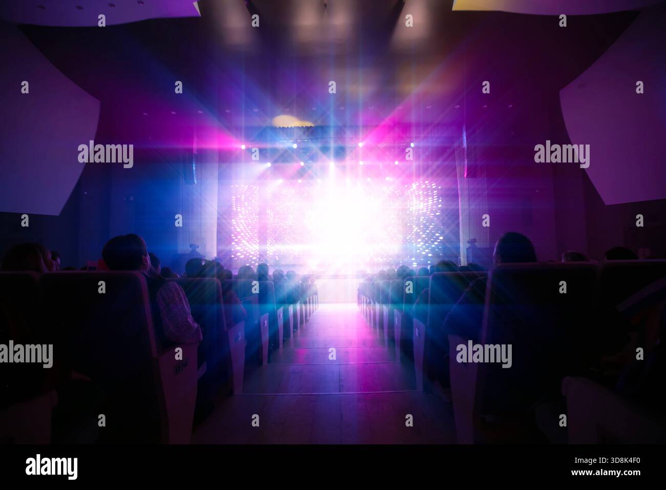 Eine lebhafte Atmosphäre erfüllt das Theater, während bunte Lichter auf die Bühne projizieren und das Publikum, das während eines Abends in Erwartung sitzt, in ihren Bann ziehen Stockfoto