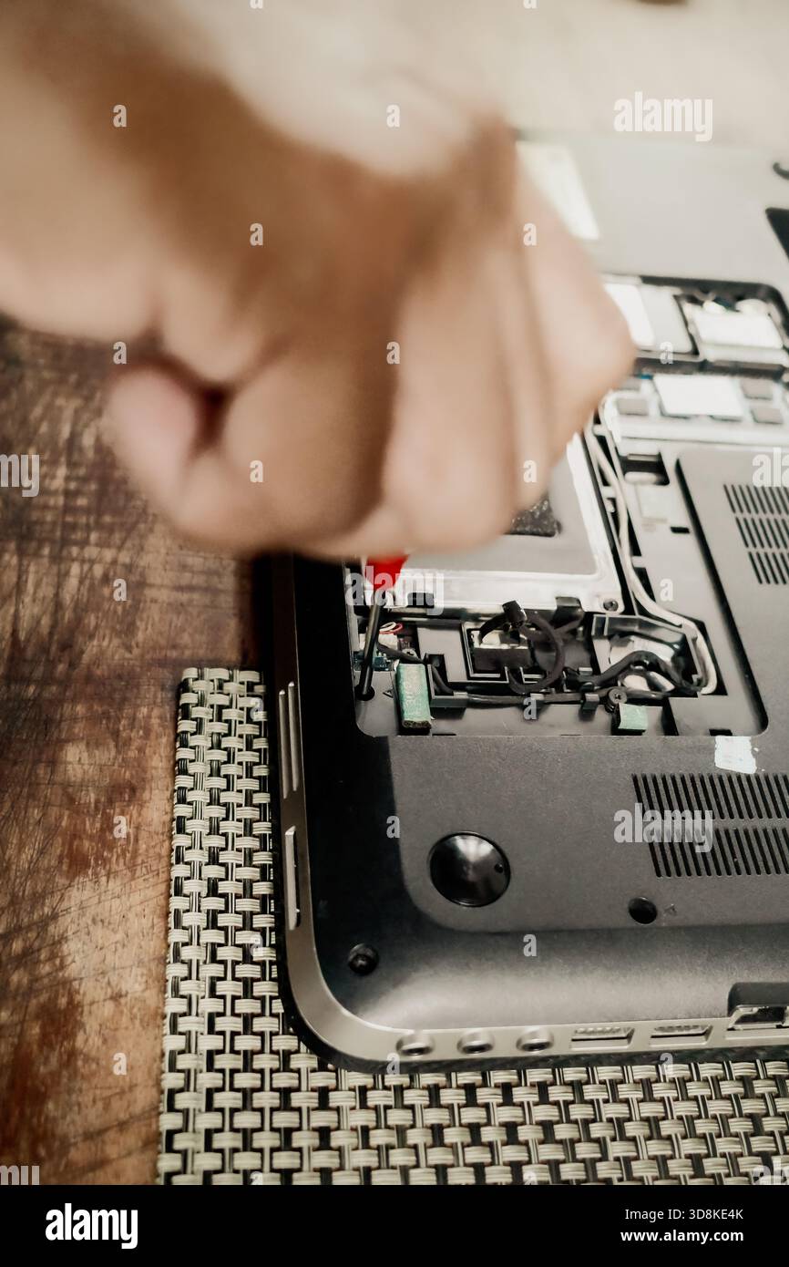 Eine männliche Person, die einen defekten Laptop mit einem Schraubendreher repariert, um die Teile der Hardwarekomponenten zu öffnen Stockfoto