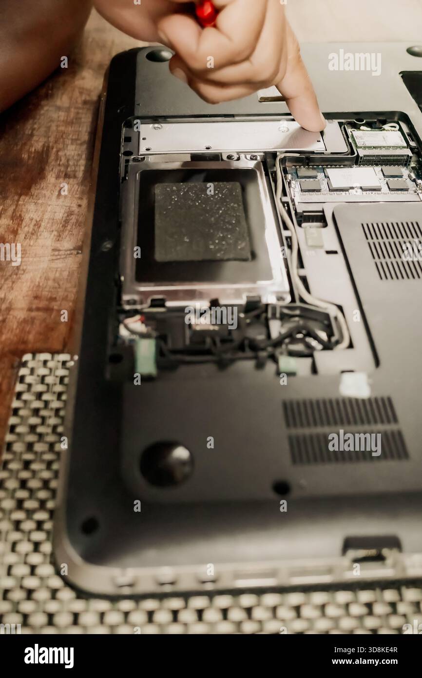 Eine männliche Person, die einen defekten Laptop mit einem Schraubendreher repariert, um die Teile der Hardwarekomponenten zu öffnen Stockfoto