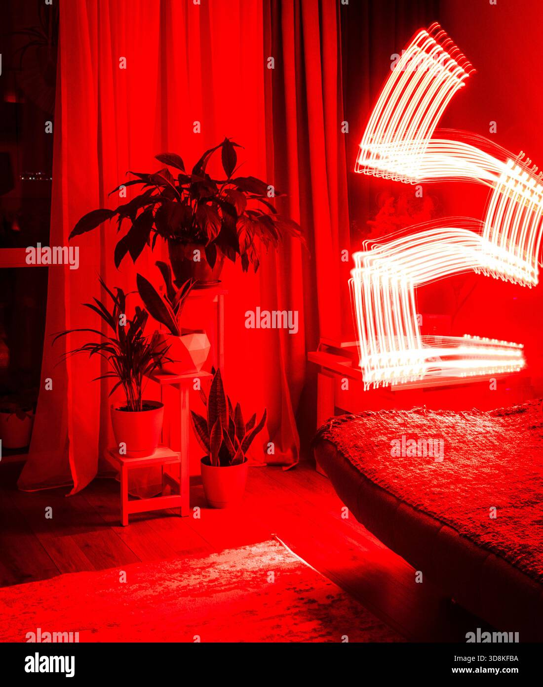 Ein Langzeitfoto, das den Weg einer sich bewegenden roten Lichtquelle in einem schwach beleuchteten Raum erfasst Stockfoto