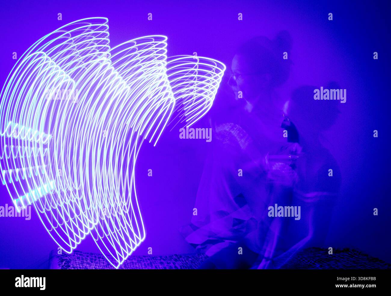 Ein Langzeitfoto, das den Weg einer sich bewegenden blauen Lichtquelle in einem schwach beleuchteten Raum erfasst Stockfoto