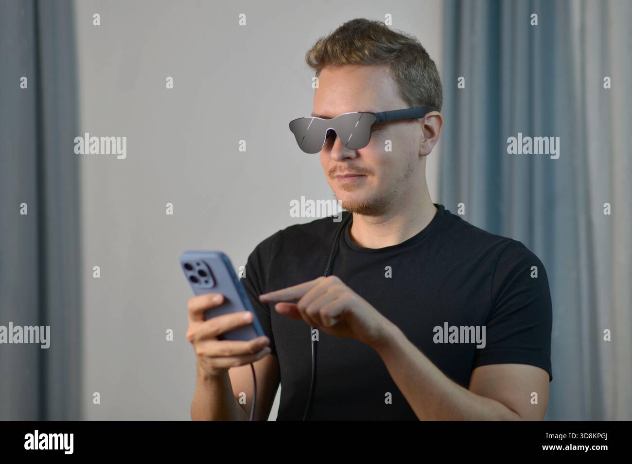 Ein junger Mann, der intelligente AR-Brillen anpasst, die mit dem Smartphone verbunden sind. Konzept der modernen Augmented Reality, intelligente Brillen, Zukunftstechnologie und digitale Limousine Stockfoto