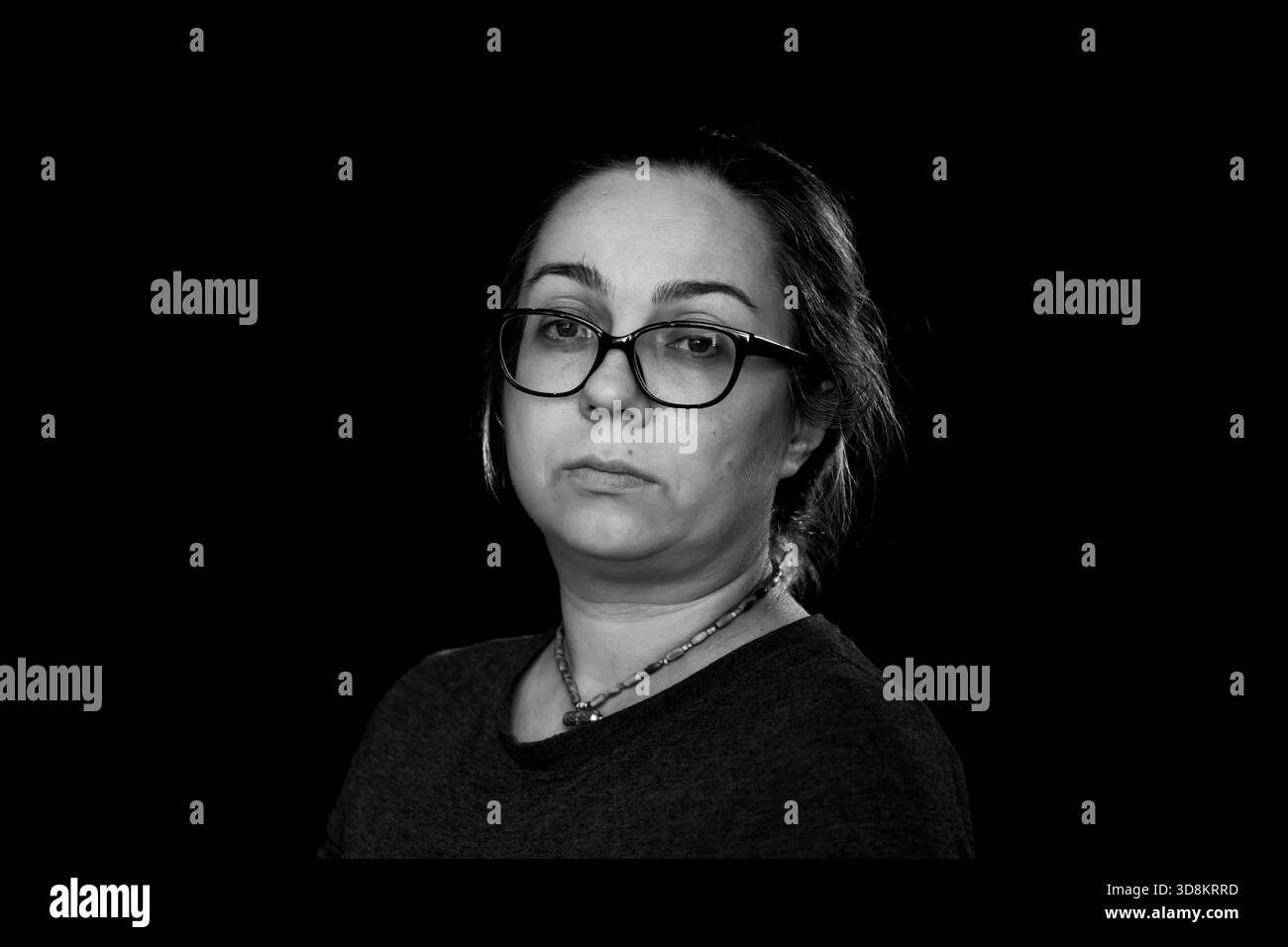 Schwarz-weißes Porträt einer Frau mit Brille auf dunklem Hintergrund mit weichem Studiolicht Stockfoto
