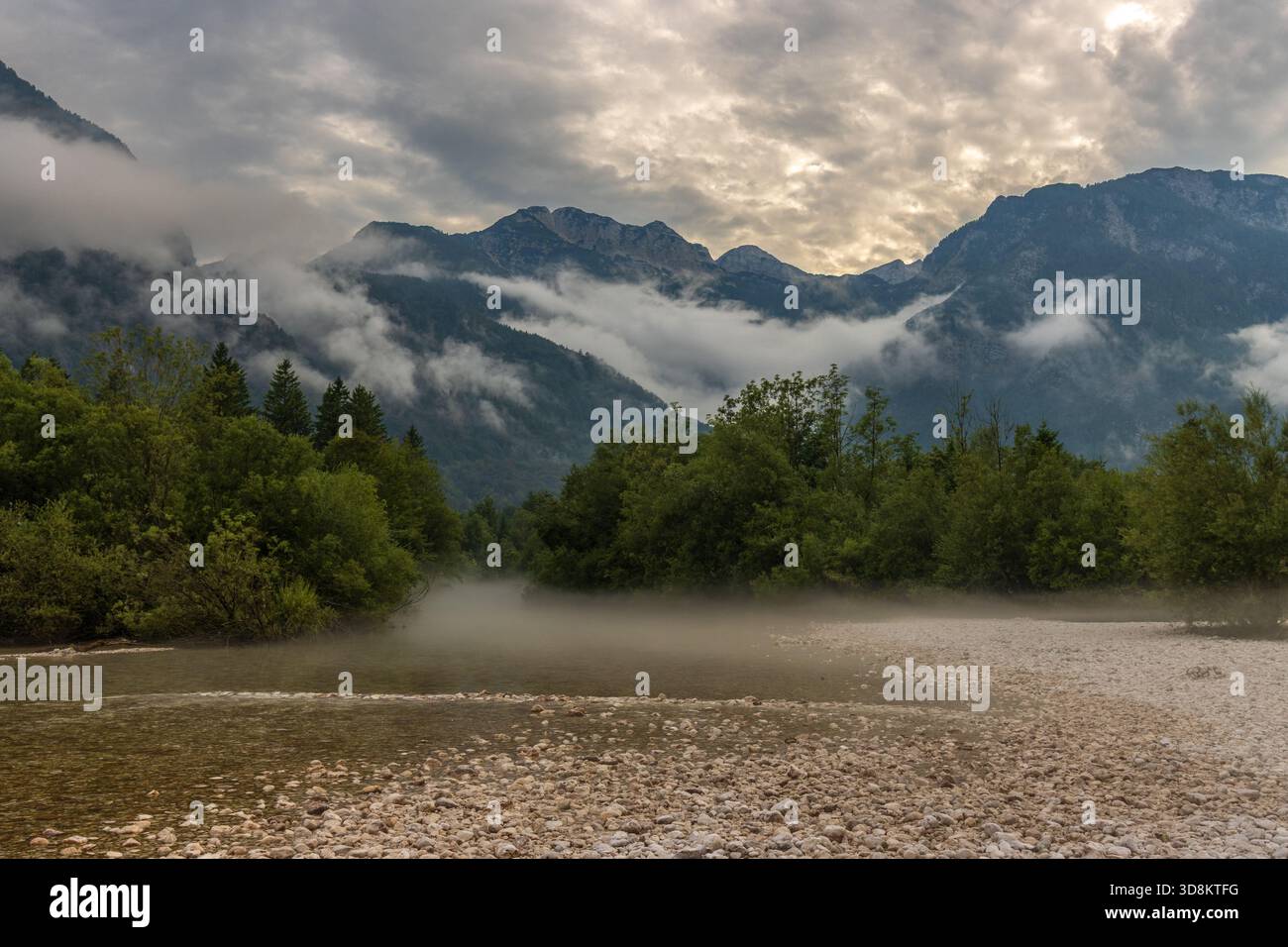 Tatmosphärisches Gebirgsflussufer mit Morgennebel und dramatischem bewölktem Himmel Stockfoto
