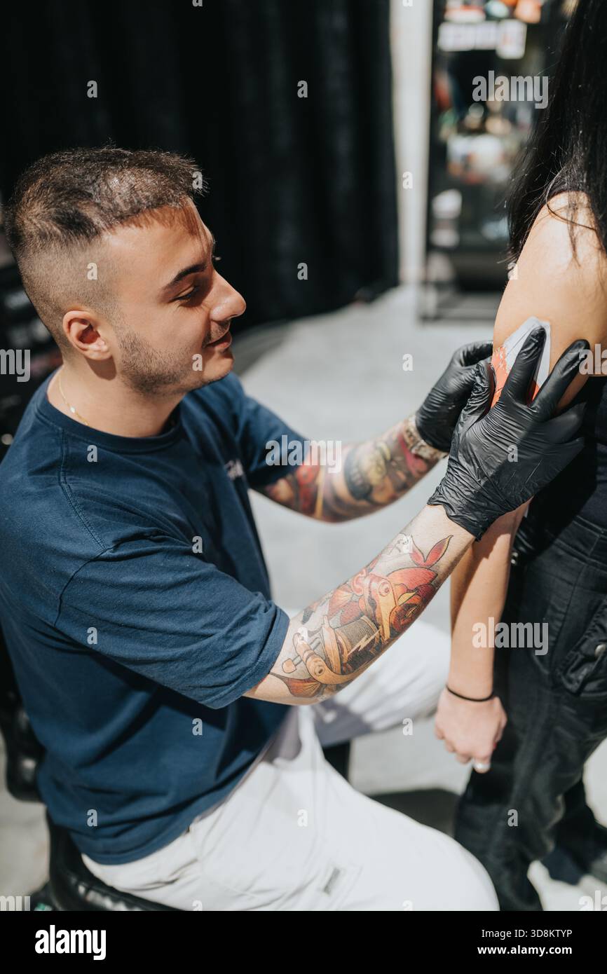 Tätowierer mit Handschuhen färbt ein Schultertätowieren auf den Kunden in einem Studio-Setting Stockfoto