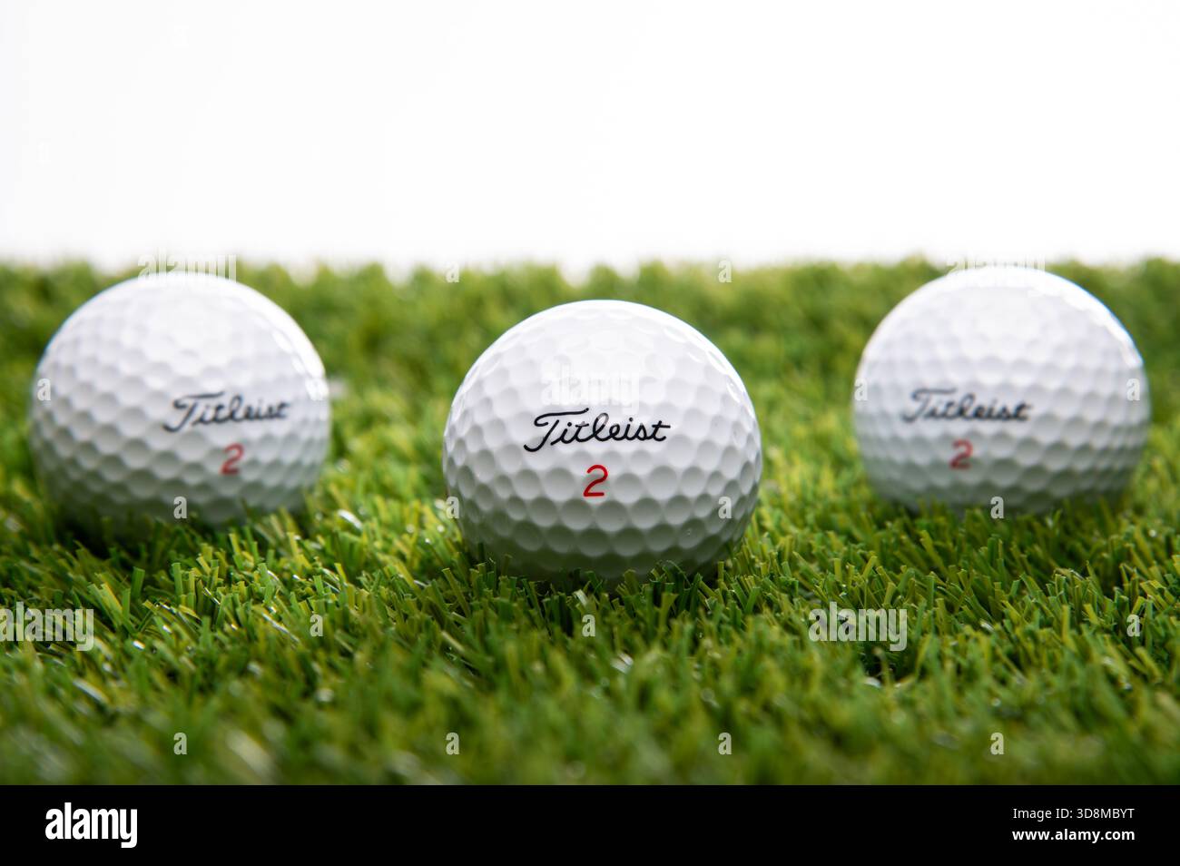 Ein Titleist 2 Golfball auf grünem Astrorasen vor weißem Hintergrund in einer Gruppe von drei nach innen gerichteten Golfbällen Stockfoto