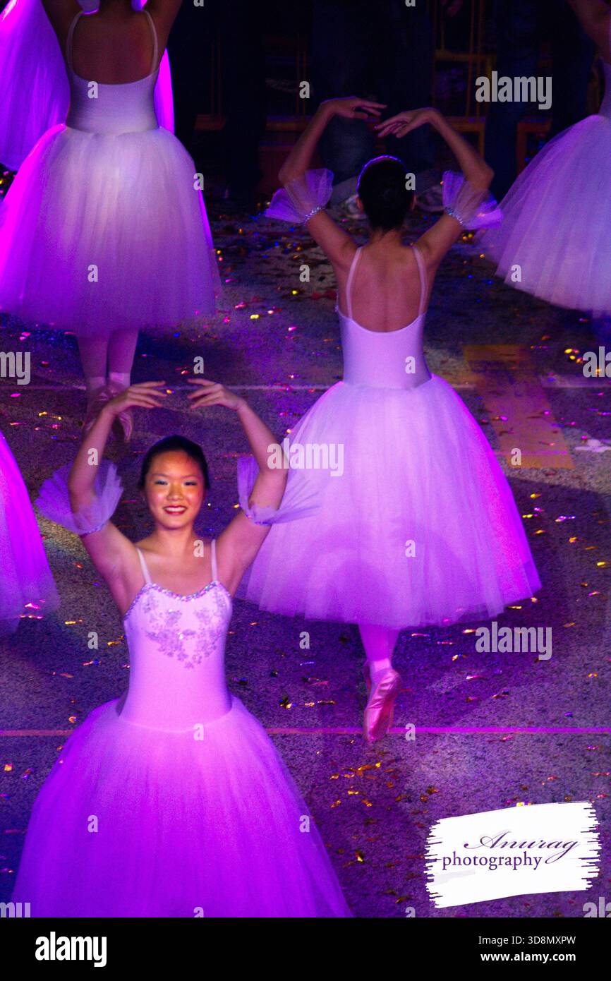 Die junge Ballerina streckt während einer Vorstellung freudig die Arme aus, umgeben von anderen Tänzern in elegantem Tutus. Stockfoto