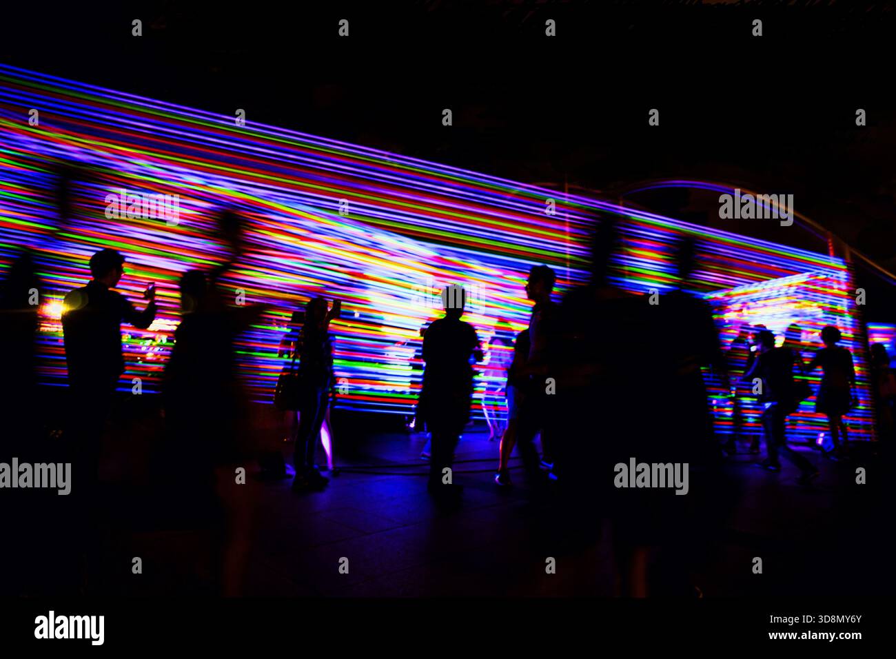 Silhouettenfiguren tanzen bei Nacht unter einer blendenden Ausstellung farbenfroher Festivallichter. Stockfoto