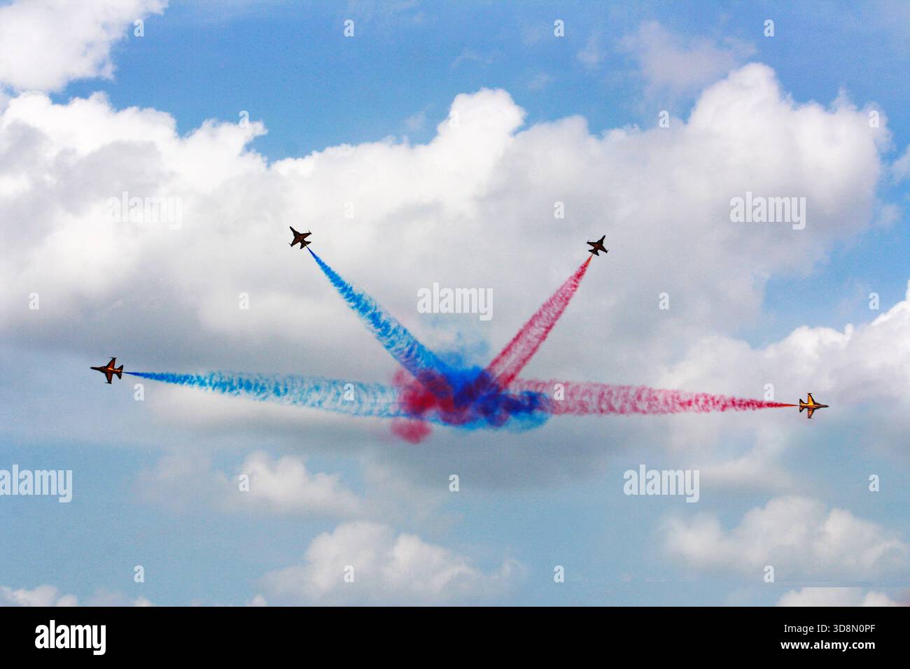 Luftjets führen ein dynamisches rot-weiß-blaues Rauchkreuzmuster vor einem Hintergrund aus weichen blauen und weißen Wolken aus Stockfoto