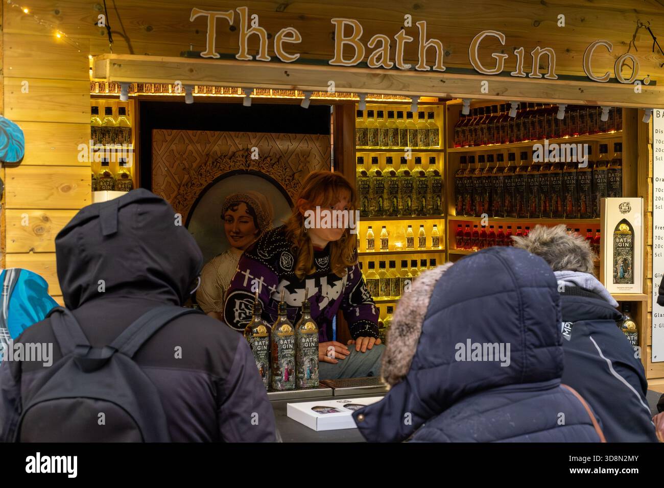 Ein Verkäufer im Bath Gin Co. Stand bedient Kunden. Der Stand ist mit verschiedenen Flaschen Gin gefüllt, und hinter dem ist ein Porträt einer Frau zu sehen Stockfoto