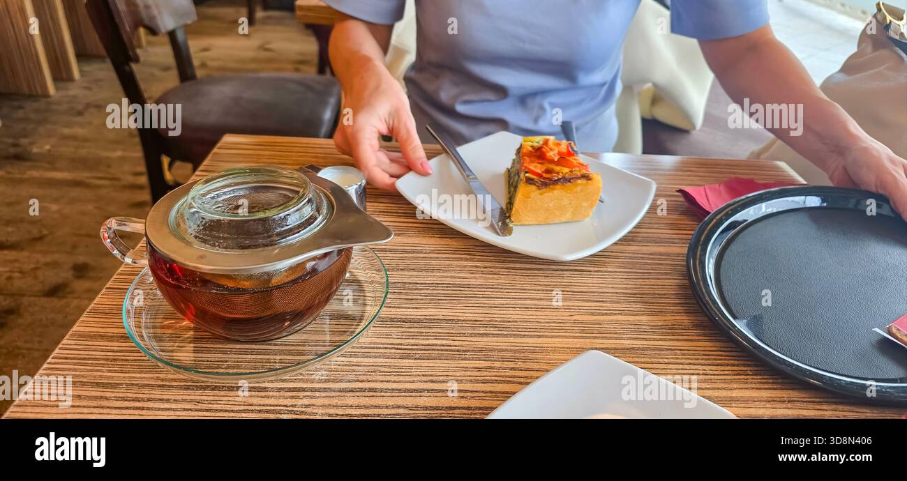 Individual serviert Tee und ein Stück Dessert in einem warmen Café mit Holztisch und einladender Atmosphäre. - Smartphone-aufgenommenes Stockfoto
