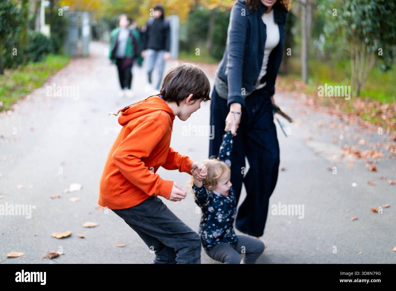 Eine glückliche Familie genießt eine gute gemeinsame Zeit, während Kinder spielerisch auf einem malerischen Waldweg laufen. Lachen erfüllt die Luft zwischen lebhaftem Herbstlaub und einer ruhigen Atmosphäre. Stockfoto