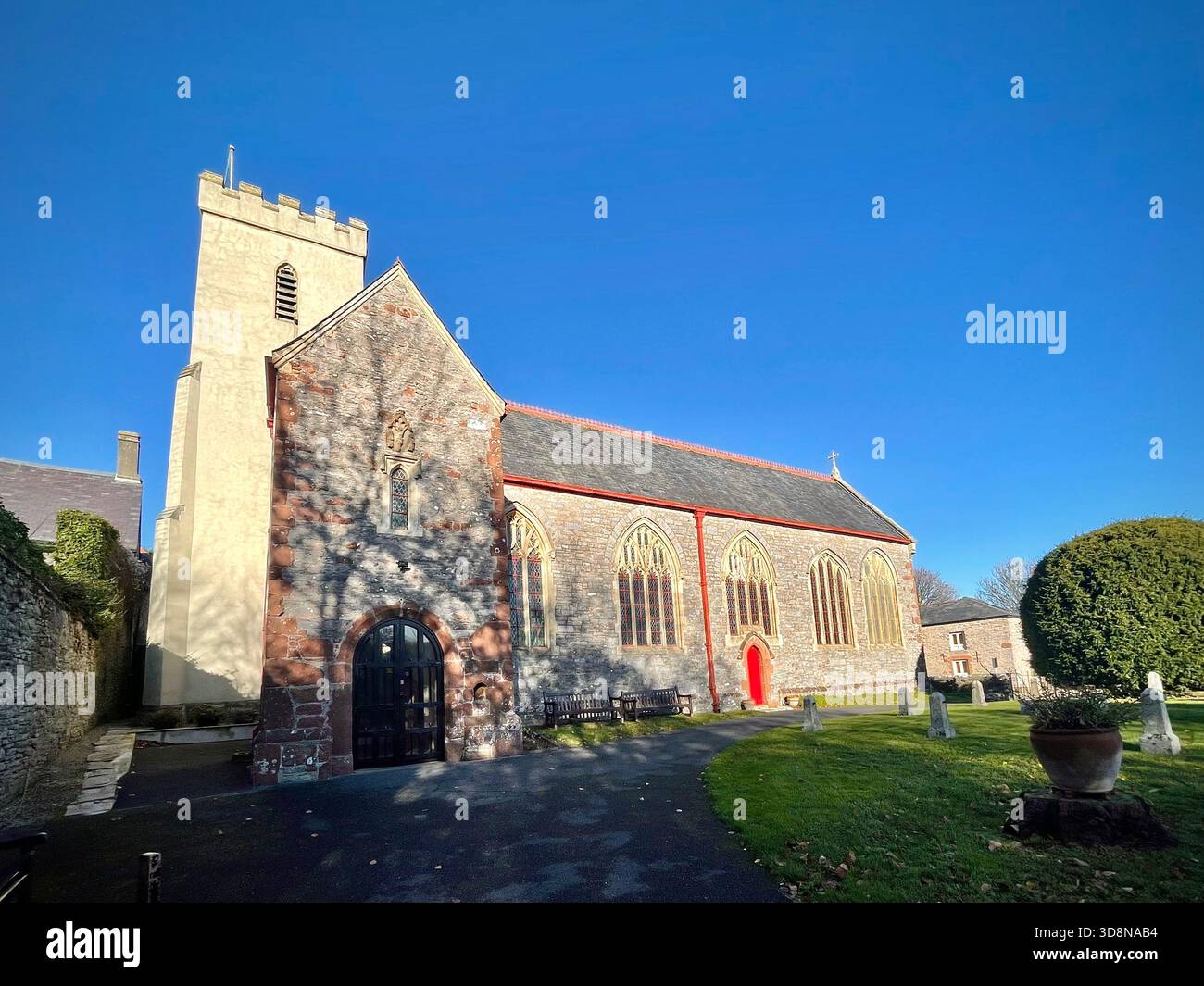 Historische Pfarrei aus Stein mit quadratischem Glockenturm und Bogenfenstern in Churston Ferrers, Devon, England, umgeben von Grabsteinen auf dem Friedhof Stockfoto