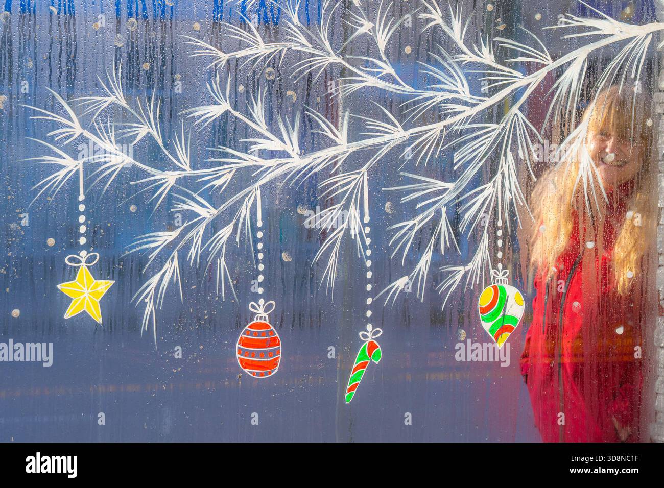Frau, die an einem Fenster mit Feiertagsdekoration vorbeiging. Stockfoto