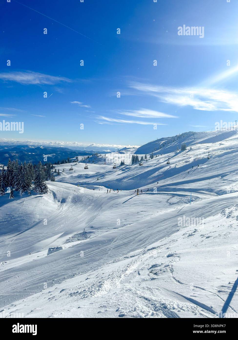Idyllischer Blick auf die schneebedeckten Pisten von Jahorina, mit Skifahrern und einem hellblauen Himmel. Ein perfekter Ort, um Wintertourismus und Aktivurlaub zu fördern Stockfoto