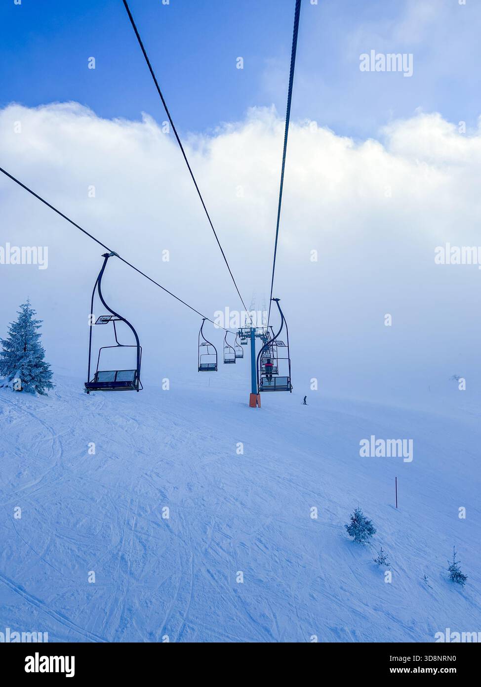 Sessellifte gleiten unter hellem Himmel und leichtem Nebel über einen verschneiten Hang auf dem Jahorina Berg und schaffen eine ruhige Wintersport- und Reiseszene. - Smartphone-aufgenommenes Stockfoto