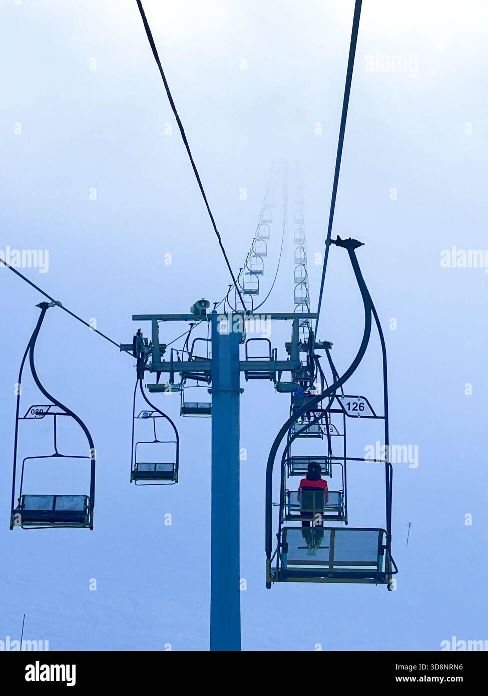 Sessellifte steigen durch den dicken Winternebel auf dem Jahorina Mountain und schaffen eine ruhige alpine Szene, die perfekt für Wintersport und Reisekonzepte ist. - Smartphone-aufgenommenes Stockfoto