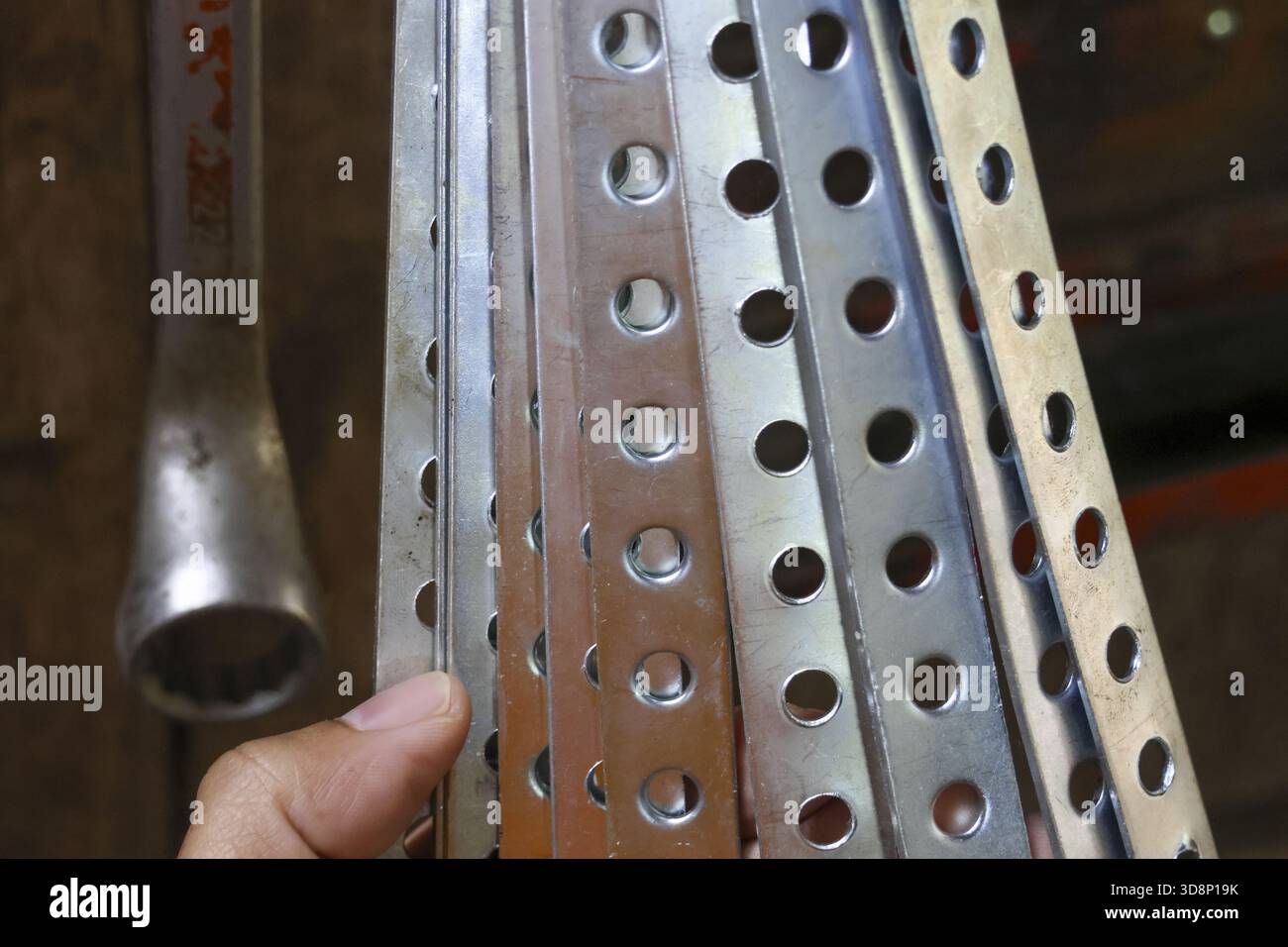 Nahaufnahme der Hand, die mehrere gelochte Stahlwinkelstangen hält. Metallisches Baumaterial mit Rundlochmuster wartet auf die Montage in der Werkstatt oder Stockfoto