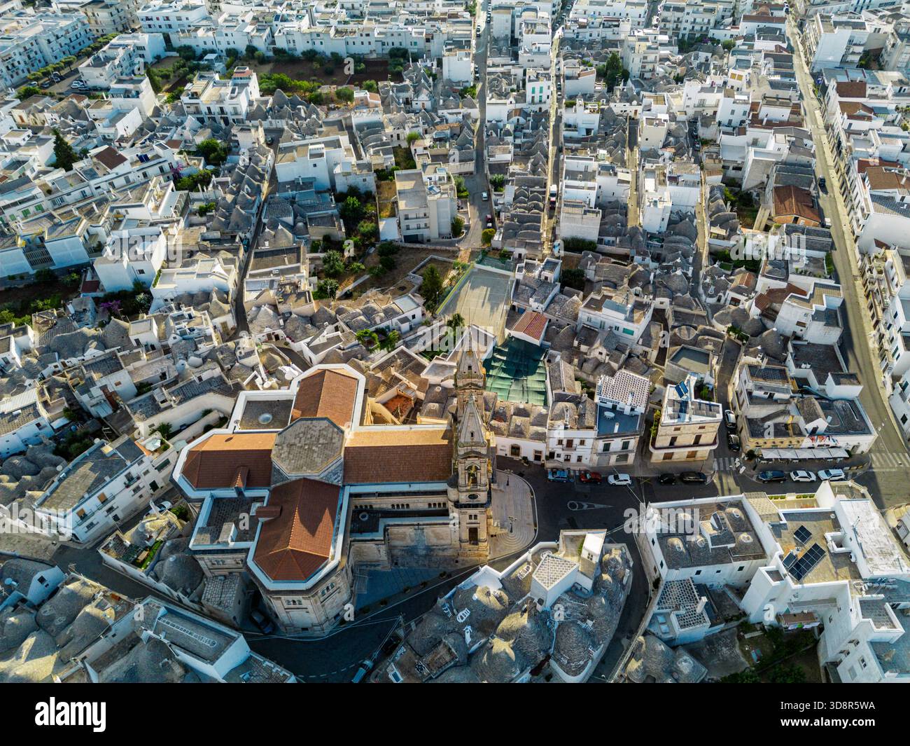 Aus der Vogelperspektive auf weiß getünchte Gebäude, die eng um eine Kirche mit einem hohen Glockenturm gruppiert sind und ein Labyrinth aus Texturen und Tönen schaffen, Alberobello, Apu Stockfoto