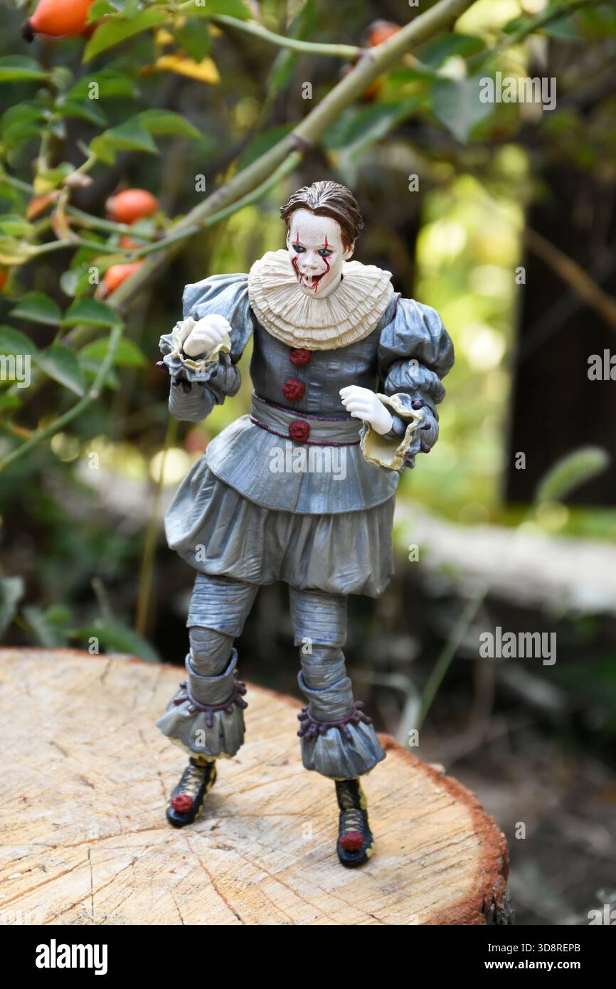 NECA Actionfigur des Pennywise Clowns aus dem Horrorfilm IT 2. Pennyway Kernschmelze im Garten, Hüftrose vor dem Hintergrund des Zauns. Stockfoto
