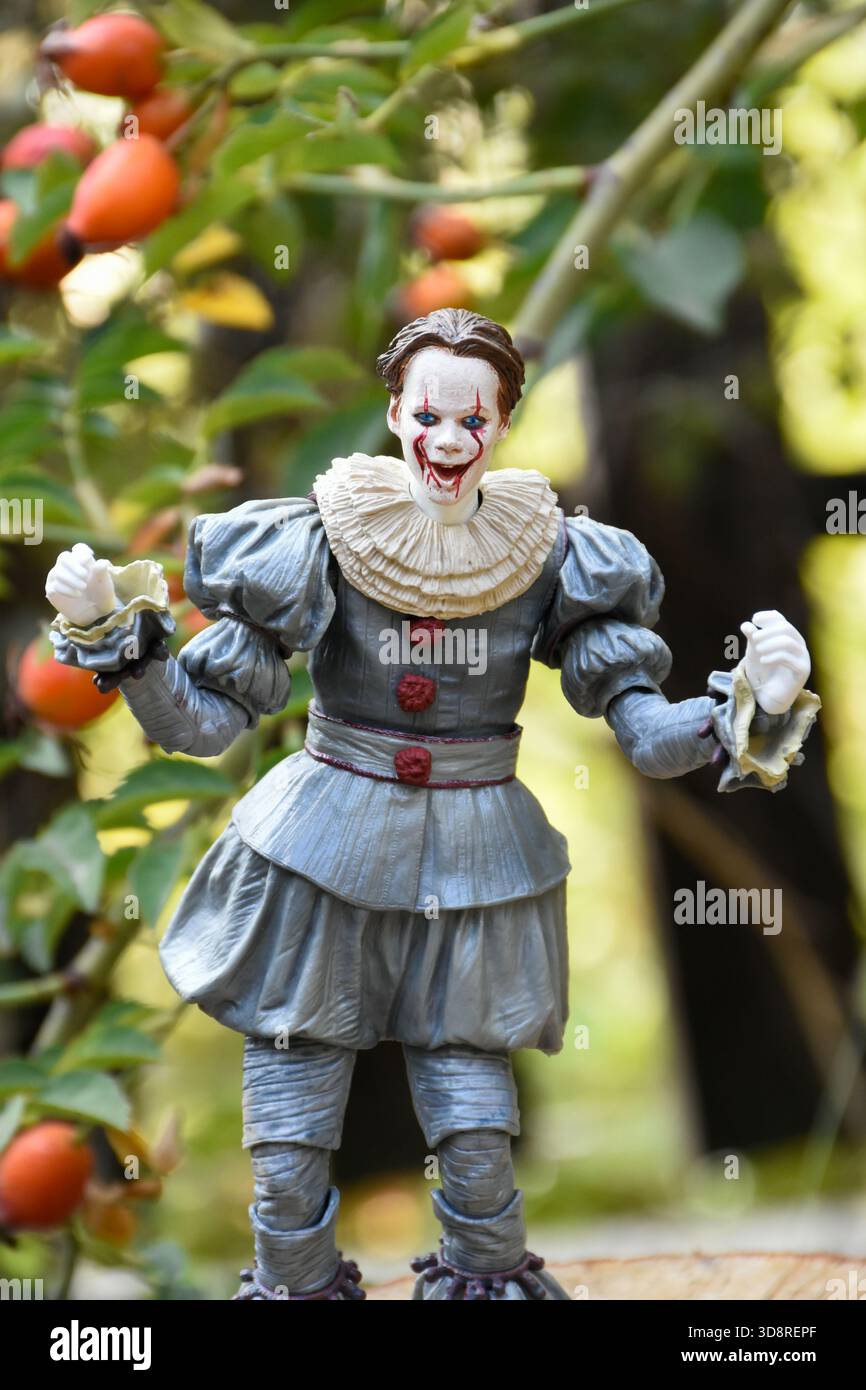 NECA Actionfigur des Pennywise Clowns aus dem Horrorfilm IT 2. Pennyway Kernschmelze im Garten, Hüftrose vor dem Hintergrund des Zauns. Stockfoto