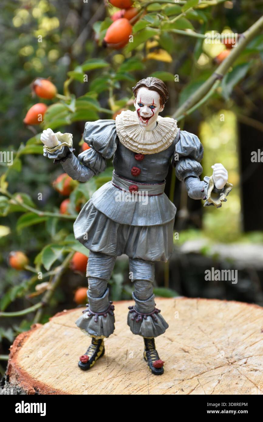NECA Actionfigur des Pennywise Clowns aus dem Horrorfilm IT 2. Pennyway Kernschmelze im Garten, Hüftrose vor dem Hintergrund des Zauns. Stockfoto