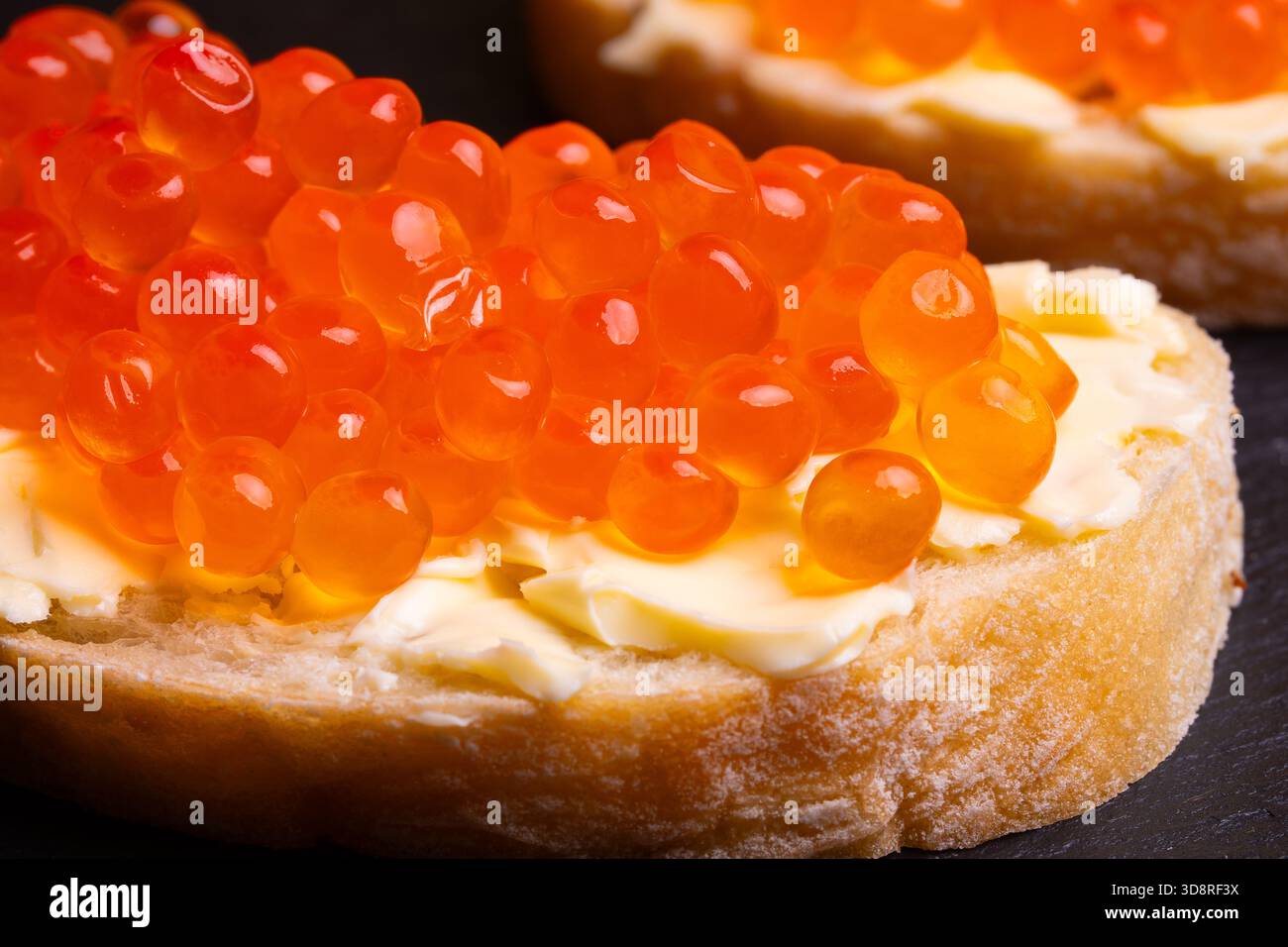 Sandwiches mit rotem Kaviar auf schwarzem Schiefersteinteller. Eine köstliche Vorspeise aus Forellenkaviar auf einer Scheibe Brot mit Frischkäse. Lachsfischrogen. Stockfoto