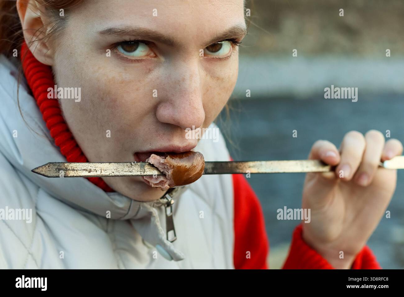 Eine Person in gemütlicher Winterausrüstung nimmt einen herzhaften Happen gegrilltes Fleisch auf einem Stock an der malerischen Wasserstraße. (85 Zeichen) Stockfoto