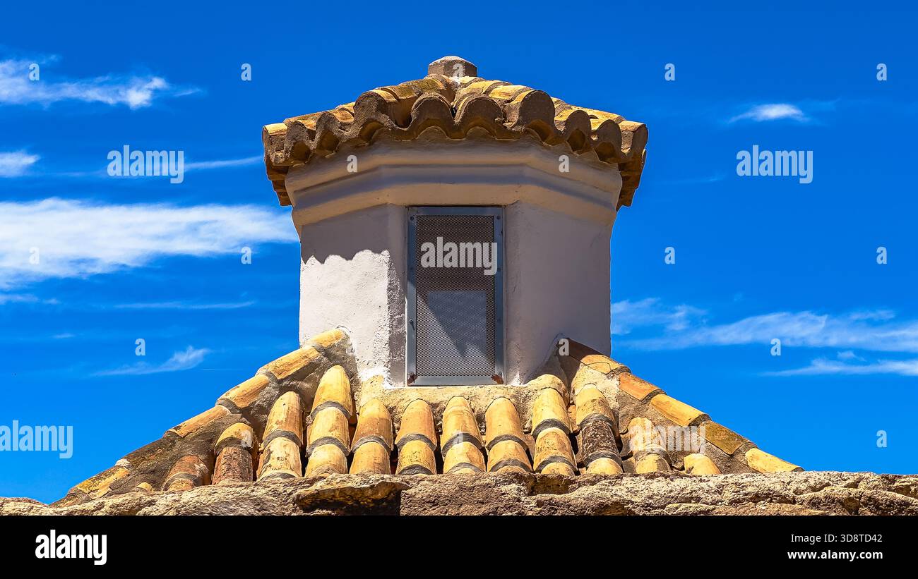 Rustikales Dach mit verwitterten Tonziegeln und kleinem Lüftungsturm vor leuchtend blauem Himmel, perfekt für Architekturkonzepte, Hintergründe und Design Stockfoto