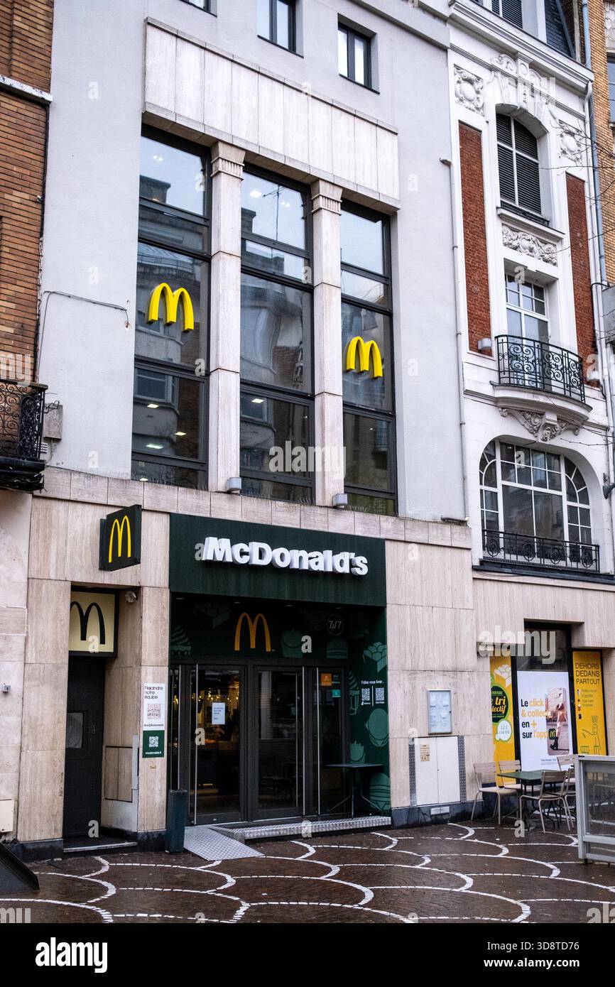Vorderansicht eines McDonalds Restauranteingangs mit beleuchteten Logos, Sitzgelegenheiten im Freien und Werbeschilderung sichtbar an der Fassade in Lille in Hauts d Stockfoto