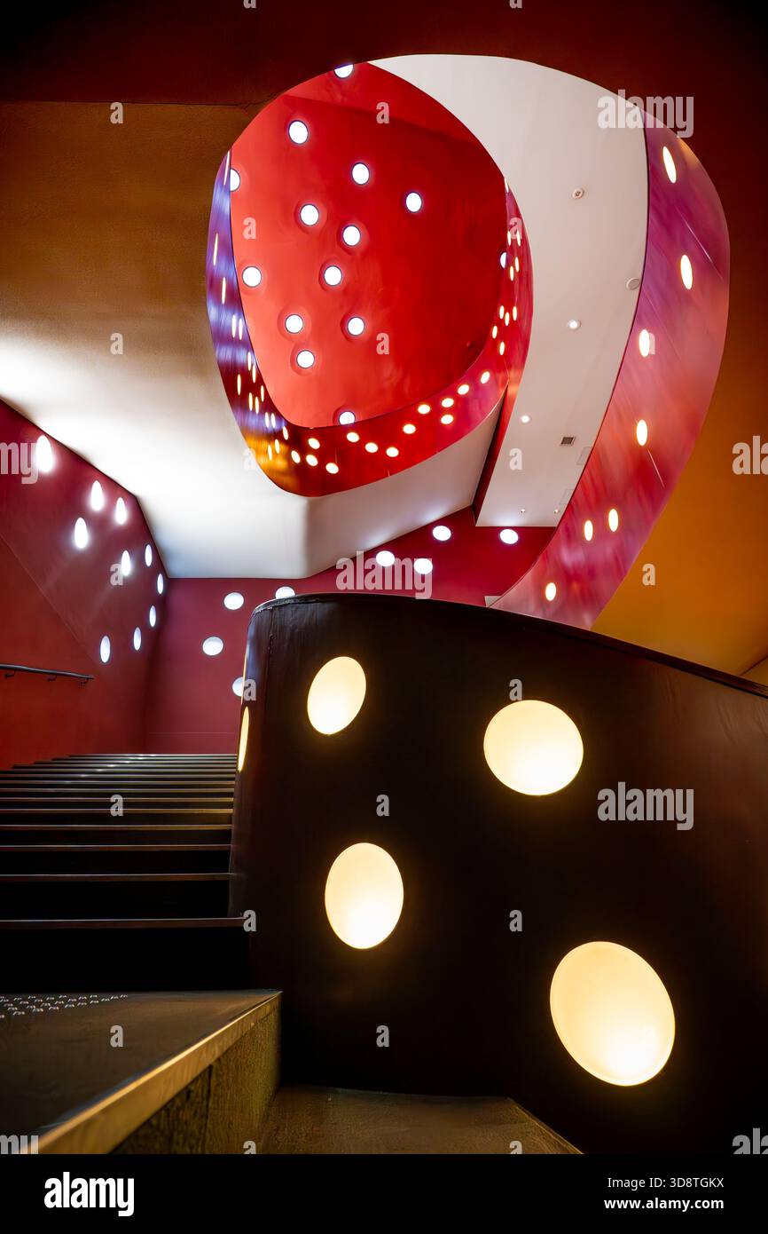 Blick auf eine moderne Treppe mit einem markanten rot-weißen, wirbelnden Design im Kontrast zu den dunklen Stufen, die einen lebendigen visuellen Rhythmus erzeugen, Sugin Stockfoto