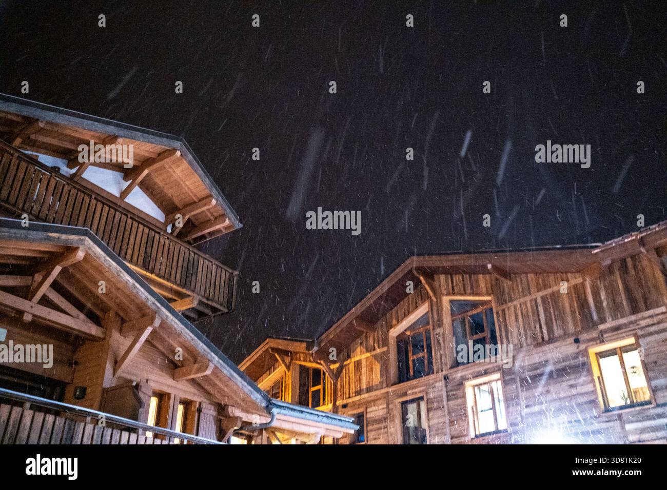 Blick auf hölzerne Wohnhäuser unter Schnee mit Nachtbeleuchtung in Les Gets in Haute-Savoie in Auvergne-Rhone-Alpes in Frankreich am 6. Januar 2024. Die Szene Il Stockfoto