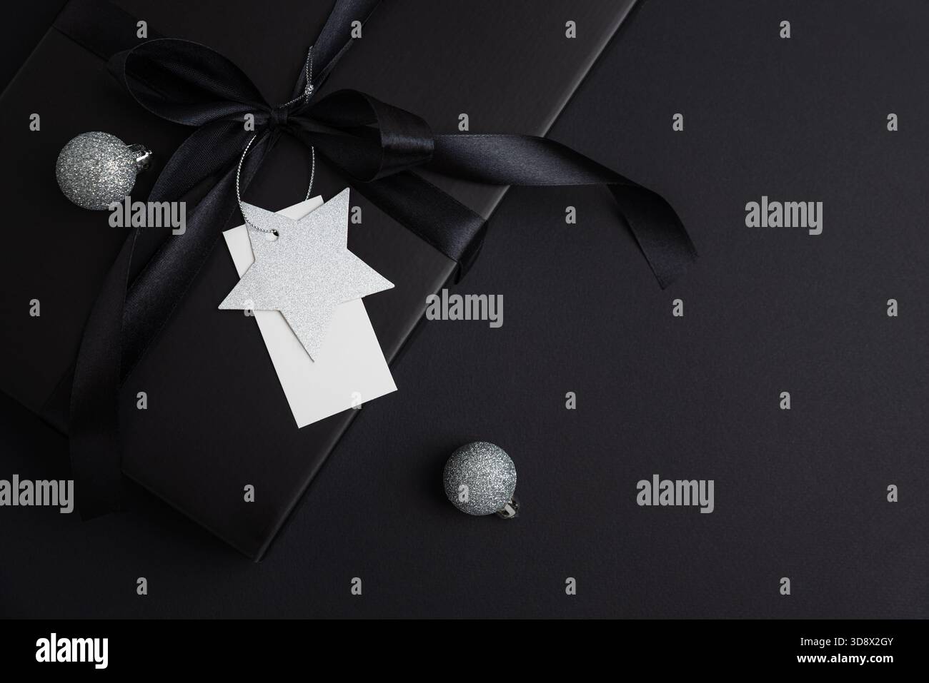 Schwarze Weihnachts-Geschenkbox mit Satinband und weißem Blanck-Etikett auf dunklem Feiertagshintergrund Stockfoto