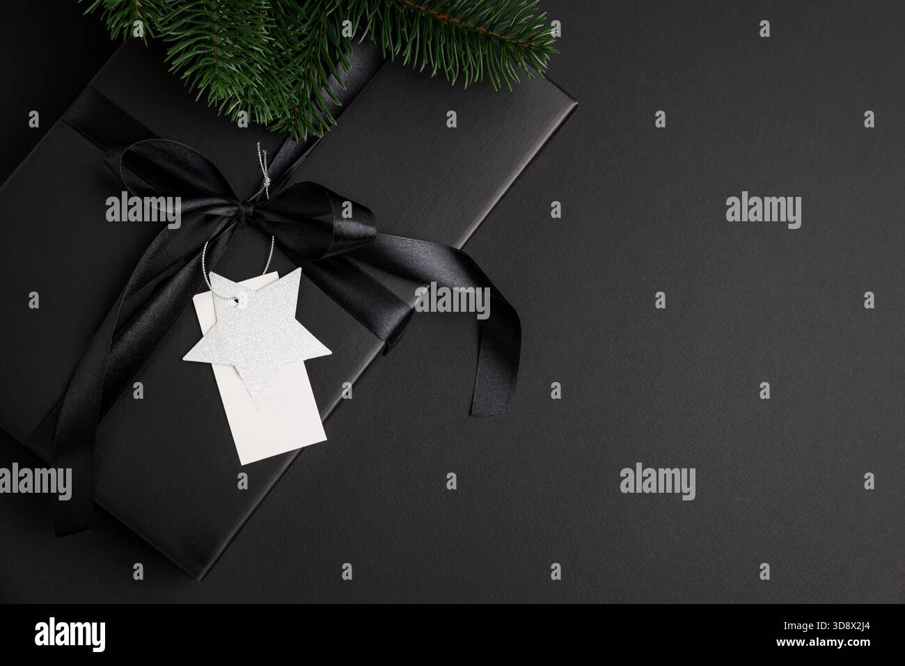 Schwarze Weihnachts-Geschenkbox mit Satinband und weißem Blanck-Etikett auf dunklem Feiertagshintergrund Stockfoto