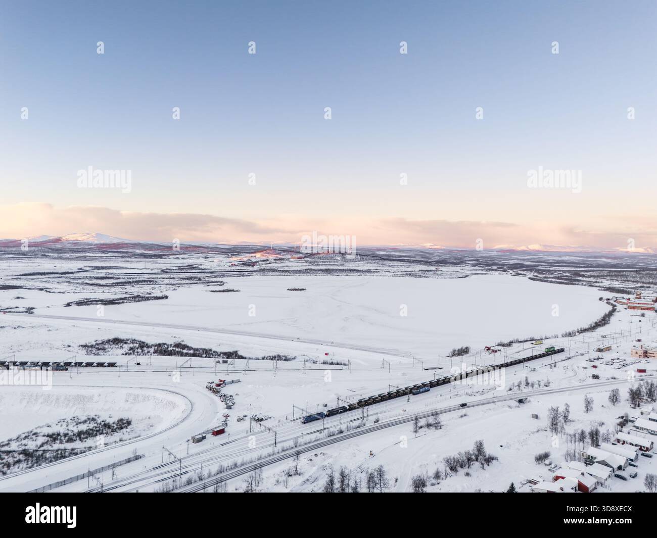 Eisenerz-Güterzug in der Nähe des Eisenerzbergwerks Kiruna, während des arktischen Winters, Windkraftwerk in der Ferne, hohe Berggipfel. Schweden Stockfoto