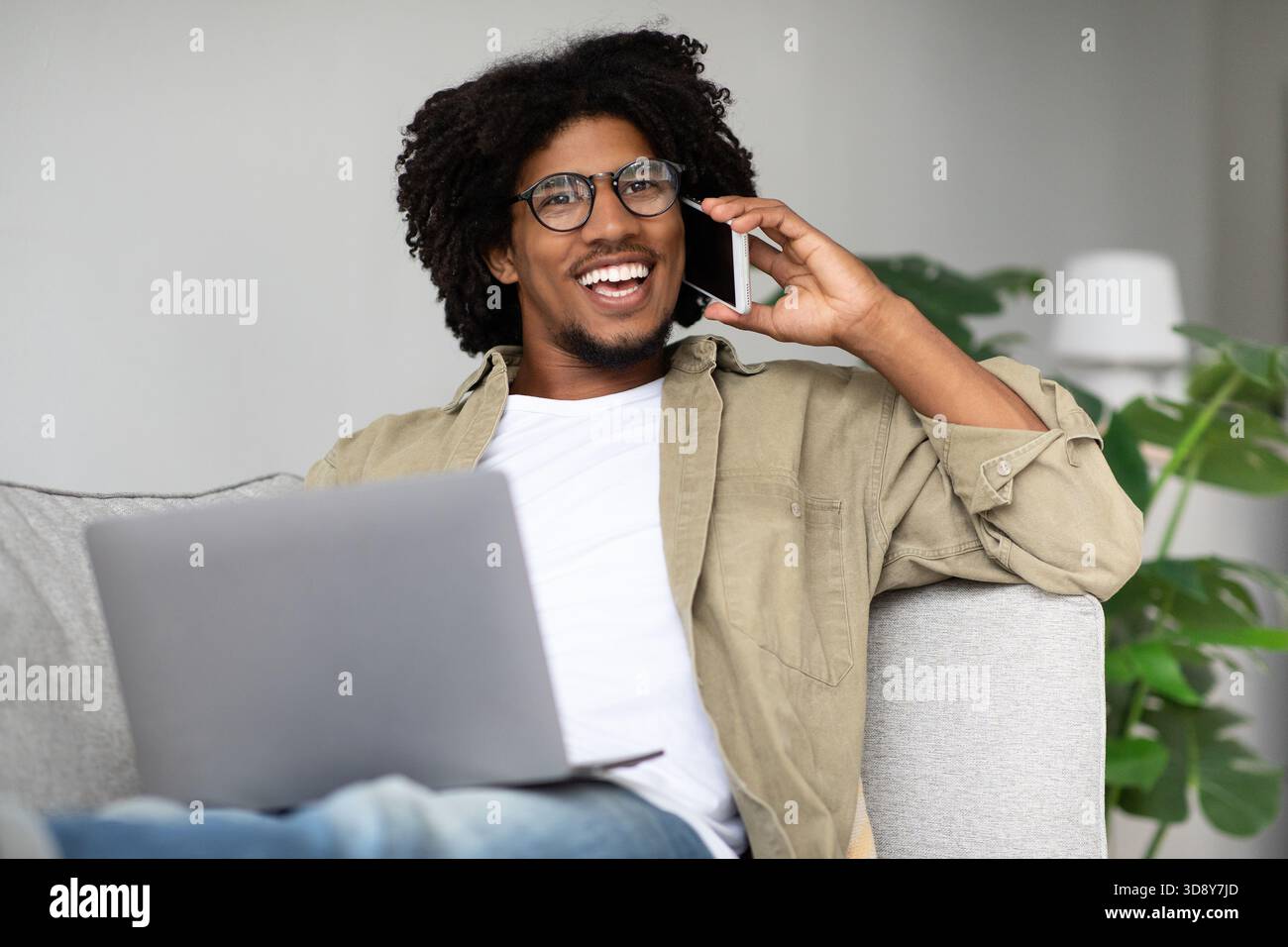 Fröhlicher Schwarzer Freelancer, der Remote-Arbeit genießt, während er im Home Office über das Mobiltelefon spricht Stockfoto