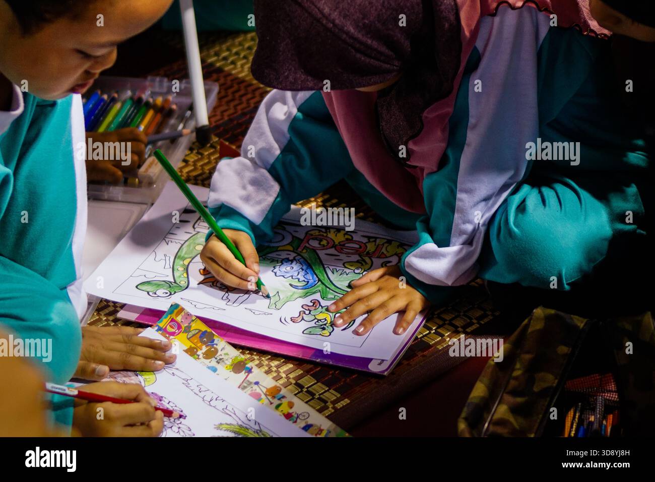 ULU KINTA, PERAK, MALAYSIA – 20. MAI 2017: Zwei malaysische Kinder in Schuluniformen färben eine Dinosaurierillustration mit Buntstiften in Innenräumen Stockfoto