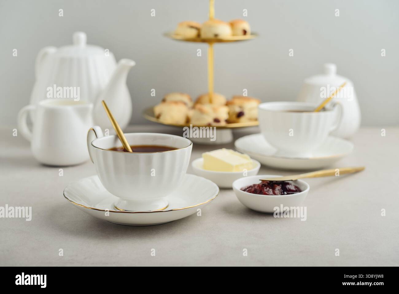Englischer Nachmittagstee in eleganten weißen Porzellantassen serviert mit Scones, Milch, Butter und Marmelade, fünf O'Clock-Tee Stockfoto