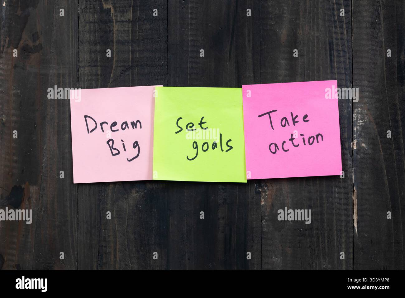 Positives Ideenkonzept mit Holztisch und Haftnotiz mit den Worten Dream Big Set Goals Take Action Stockfoto