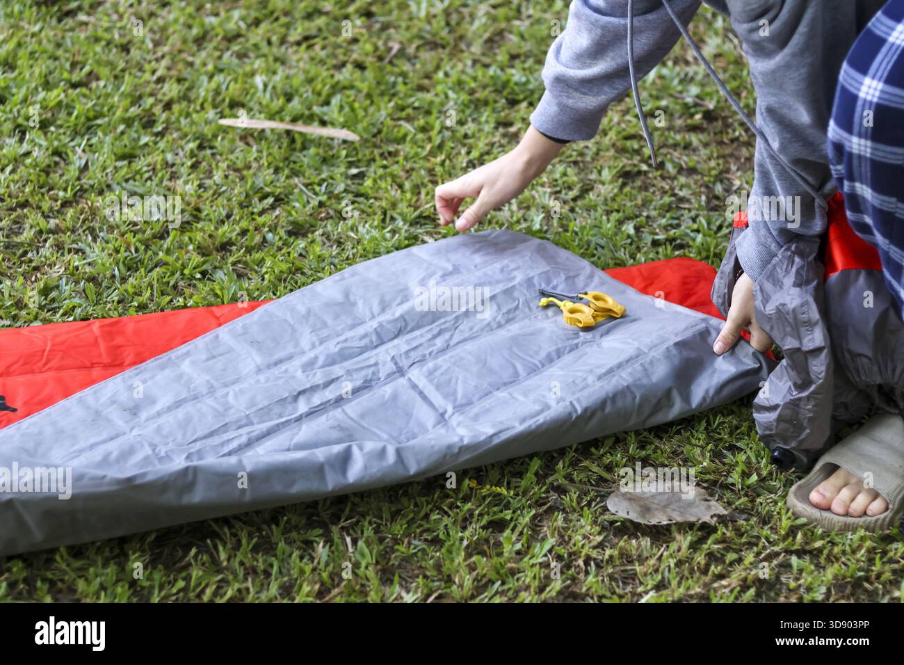 Fokussierte Person, die graue Luftmatratze auf grünem Gras für Camping-Abenteuer im Freien vorbereitet. Einrichtung einer bequemen Schlafkissen für entspannende Ni Stockfoto
