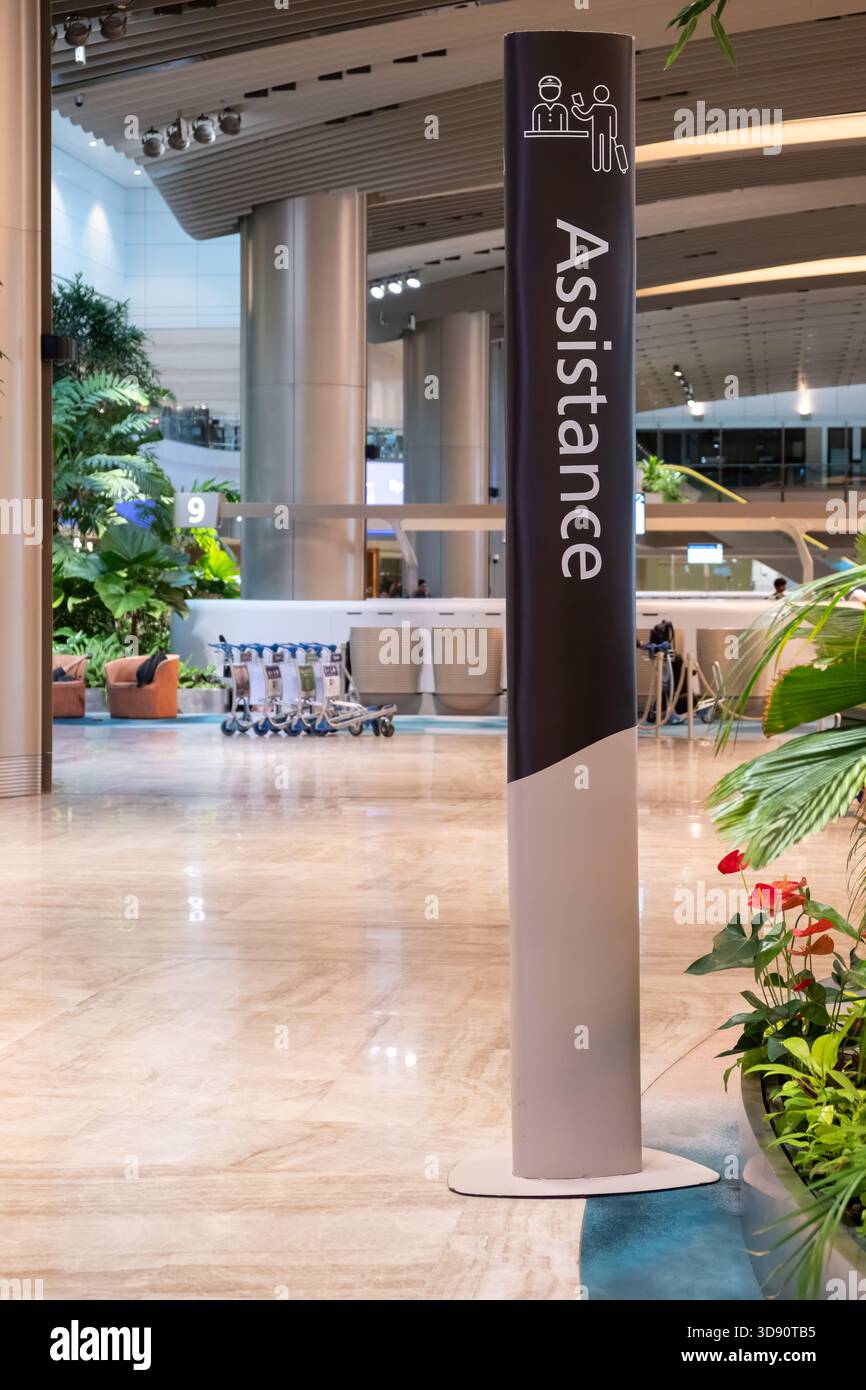 Singapur, Singapur - 02. November 2024: Das Schild „Assistance“ steht am Flughafen Changi, eingerahmt von lebendigen Pflanzen und elegantem Terminal-Design Stockfoto