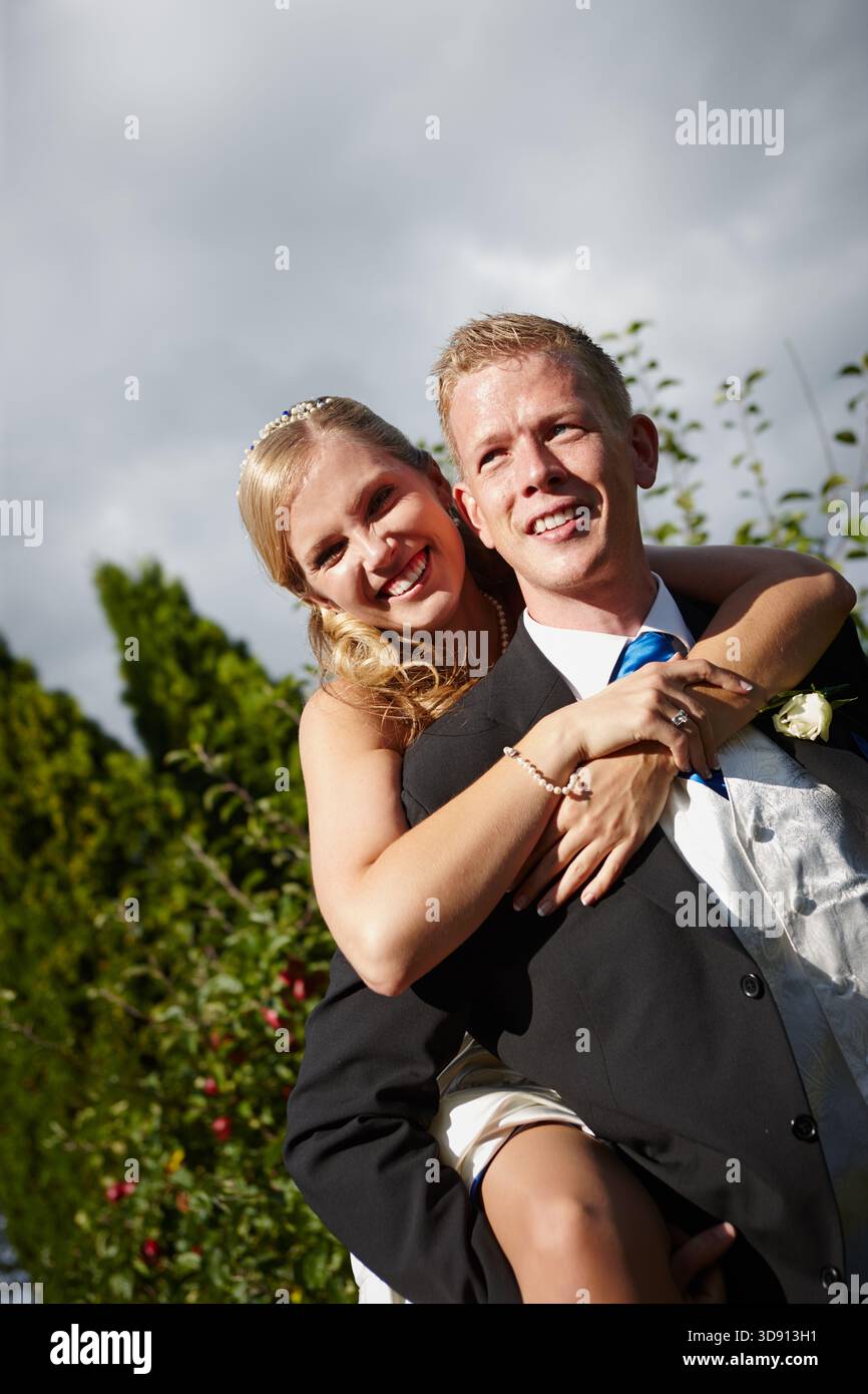 Lächeln, Paare und Huckepack bei der Hochzeit im Freien für Liebe, Feier und Heiratsverpflichtung. Porträt, Menschen und verspielte Tradition für Romantik Stockfoto