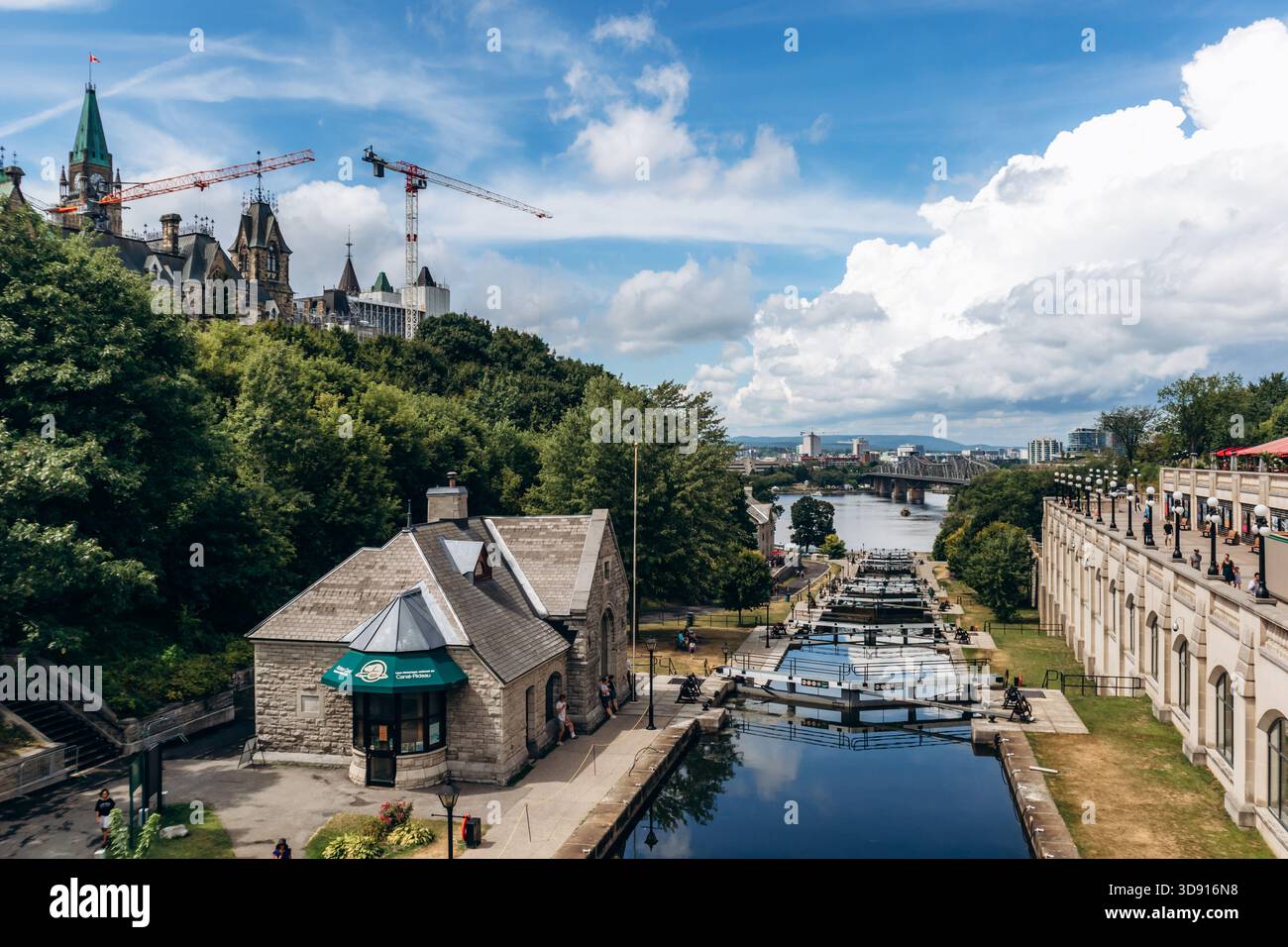 Ottawa, Kanada - 13. August 2025: Großer Blick auf die Schleusen des Rideau Canal mit Steinhäusern, Wegen und Menschen, die am Wasser entlang laufen, mit dem Ott Stockfoto
