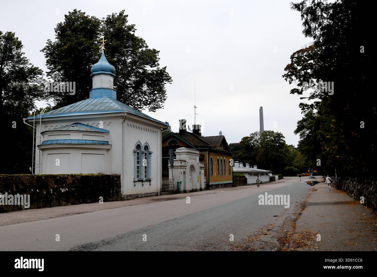 Kleine weiße Kapelle mit blauer Kuppel und Kreuz steht neben gelbem Holzhaus und langem weißen Nebengebäude in einer ruhigen Straße im städtischen Helsinki, Finnland. Stockfoto